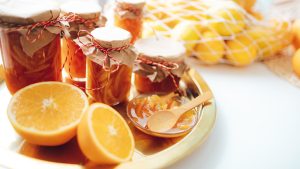Glas med hjemmelavet marmelade lukket med papir og snor, ved siden af friske appelsiner