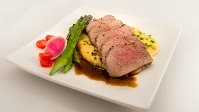 Svinemørbrad skåret i skiver med lyserød midte, serveret med sauce og asparges