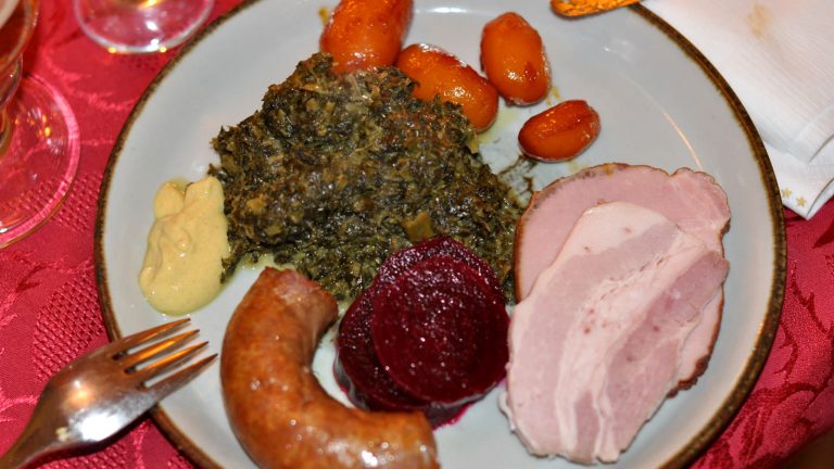 Skiver af hamburgerryg med grønlangkål, brunede kartofler, rødbeder, sennep og medisterpølse på en tallerken