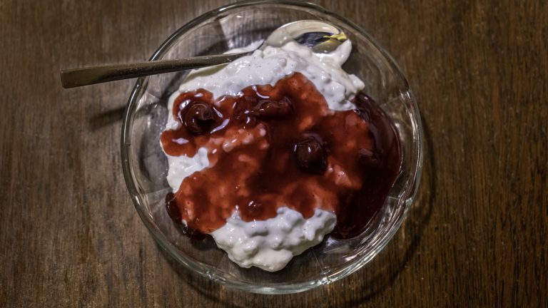 Risalamande med varm kirsebærsovs i en glasskål på et træbord — dessert juleaften