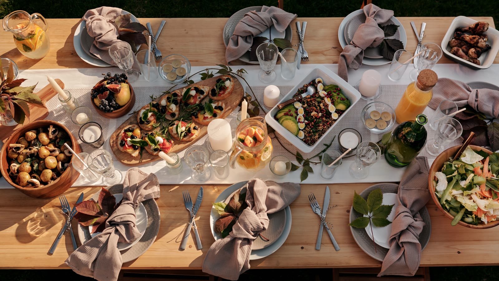Festbord set fra oven med kartofler, salat, bruschetta og kyllingelår på et langt træbord