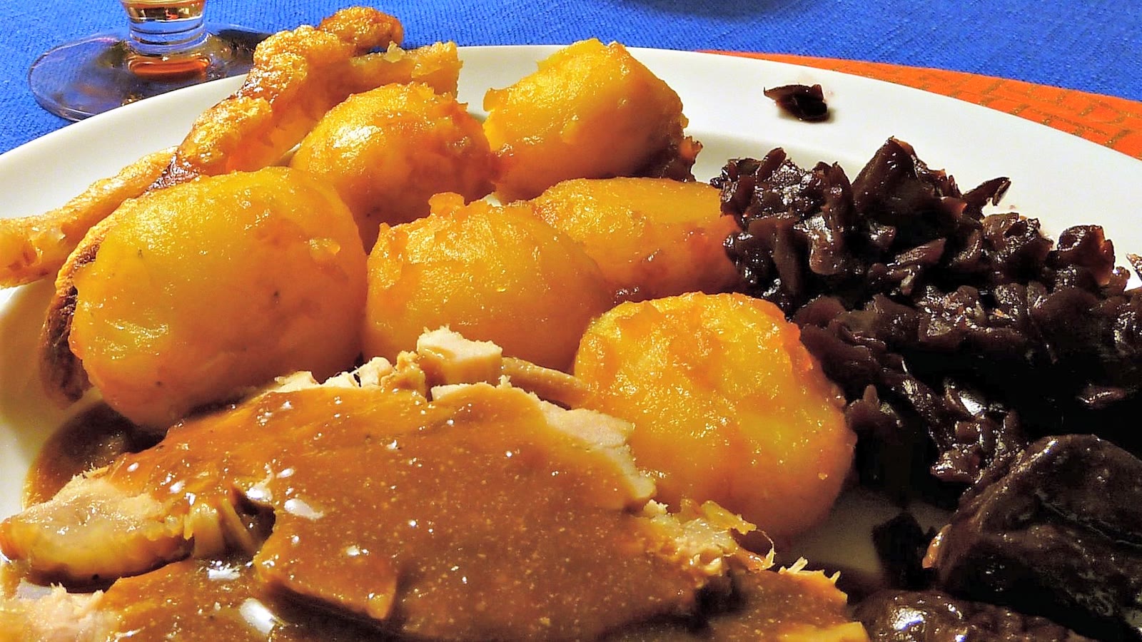 Flæskesteg med brunede kartofler, rødkål og brun sovs på en tallerken